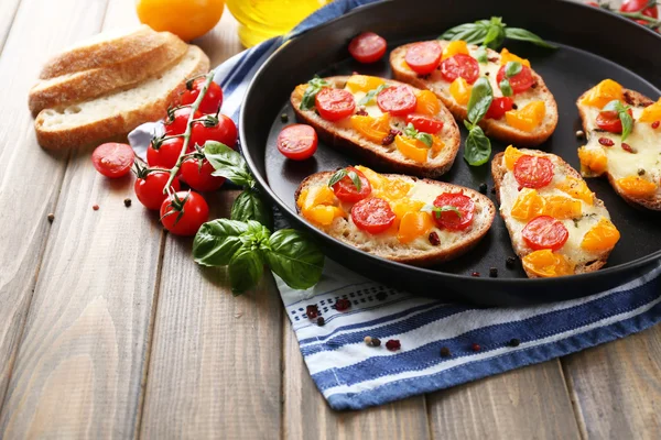 Sabroso bruschetta con tomates en la cacerola, en la mesa de madera vieja — Foto de Stock