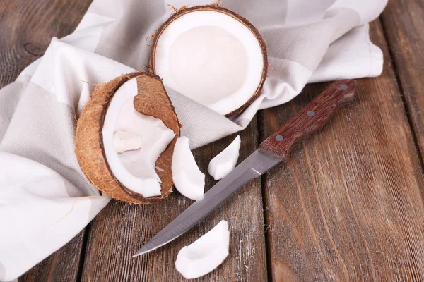 Сломанный кокос с ножом и салфеткой на деревянном фоне — стоковое фото