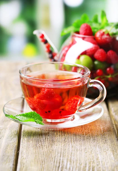 Plody červené čaj lesní plody ve sklenici, na dřevěný stůl, na světlé pozadí — Stock fotografie