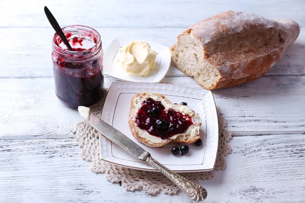 Fresh bread with homemade butter and blackcurrant jam on plate, on light wooden background — Stock Photo, Image