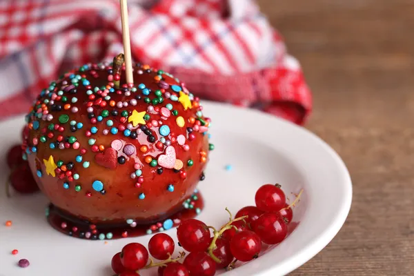 Sweet caramel apple on stick with berries, on wooden table — Stock Photo, Image