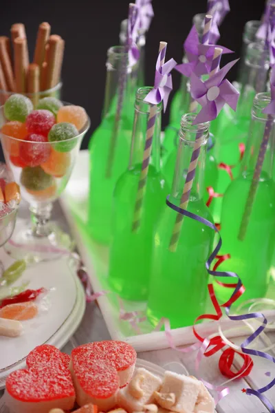 Bottles of drink with straw and sweets on dark background — Stock Photo, Image