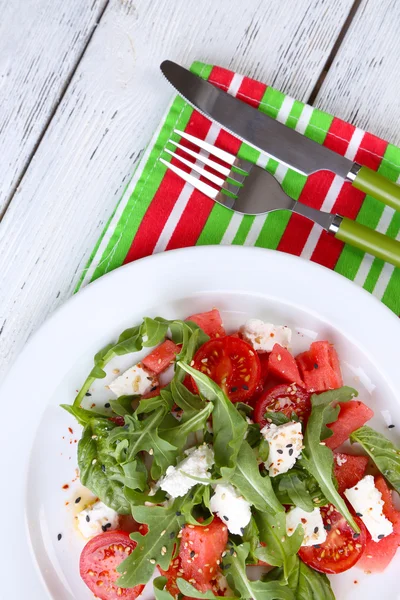 Salada com melancia, tomates, feta, rúcula e manjericão folhas no prato, no fundo de madeira — Fotografia de Stock