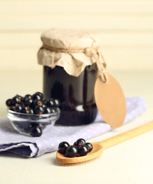 Reife schwarze Johannisbeeren in Schale und Glas mit leckerer Marmelade auf hellem Holzhintergrund. — Stockfoto
