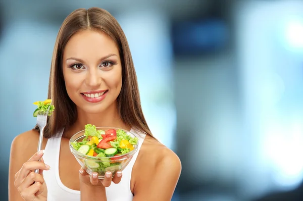 Mooie jonge vrouw met salade op interieur achtergrond — Stockfoto