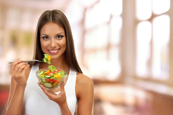 Hermosa joven con ensalada en el fondo interior —  Fotos de Stock