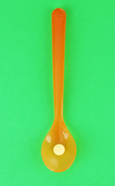 Cucchiai di plastica con pillole di colore su sfondo verde — Foto Stock