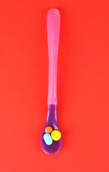 Plastic spoons with color pills on red background — Stock Photo, Image