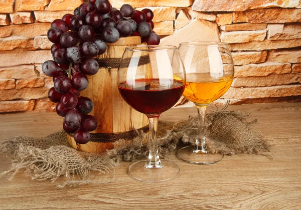 Composition of wine and grapes on wooden barrel on table on brick wall background — Stock Photo, Image