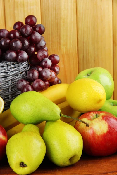 Composition of different fruits with basket on table on wooden background — Stock Photo, Image