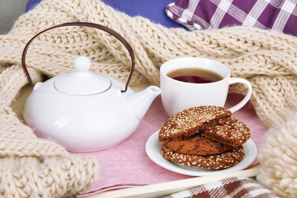 Cup and teapot with cookies on tray and scarf on bed close up — Stock Photo, Image