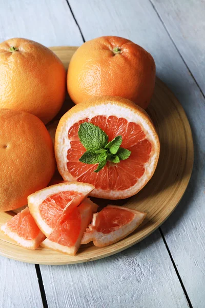 Reife Grapefruits auf Teller auf farbigem Holzhintergrund — Stockfoto