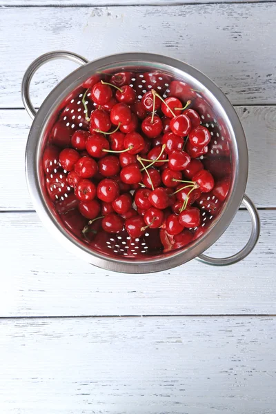 Sweet cherries in colander on color wooden background — Stock Photo, Image