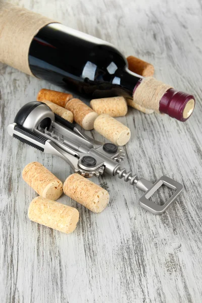 Sacacorchos con tapones de vino y botella de vino sobre mesa de madera —  Fotos de Stock