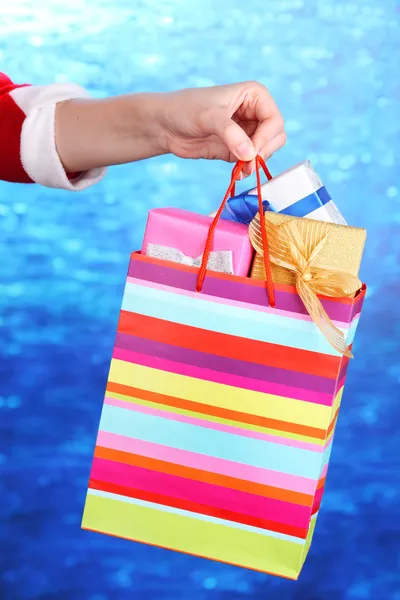 La mano sostiene el paquete con regalos de Año Nuevo sobre fondo azul — Foto de Stock