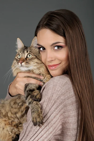 Krásná mladá žena hospodářství kočka na šedém pozadí — Stock fotografie