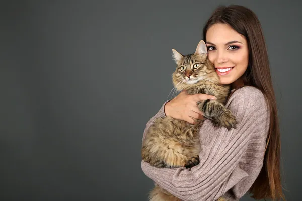 Bella giovane donna che tiene il gatto su sfondo grigio — Foto Stock