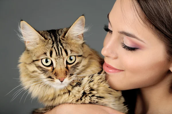 Hermosa mujer joven sosteniendo gato sobre fondo gris — Foto de Stock