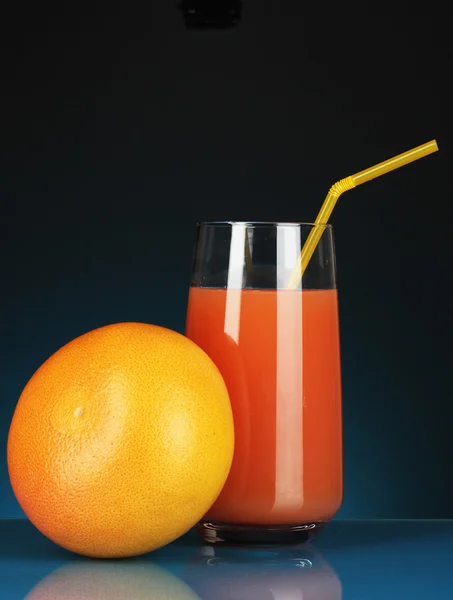 Delicioso zumo de pomelo en vaso y pomelo junto a él sobre fondo azul oscuro —  Fotos de Stock