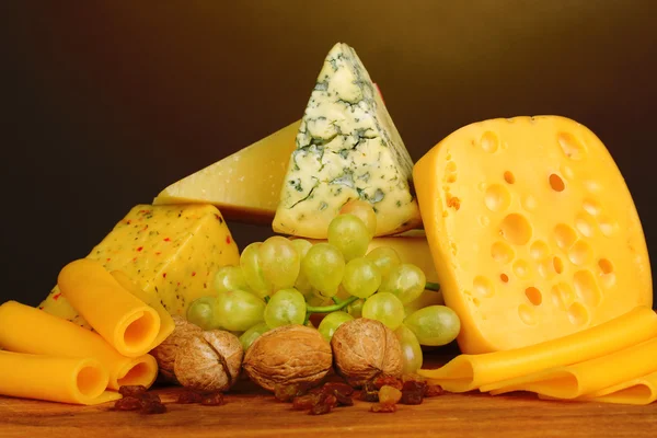Various types of cheese on wooden table on brown background — Stock Photo, Image