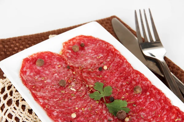 Tasty salami on plate on  napkin isolated on white — Stock Photo, Image