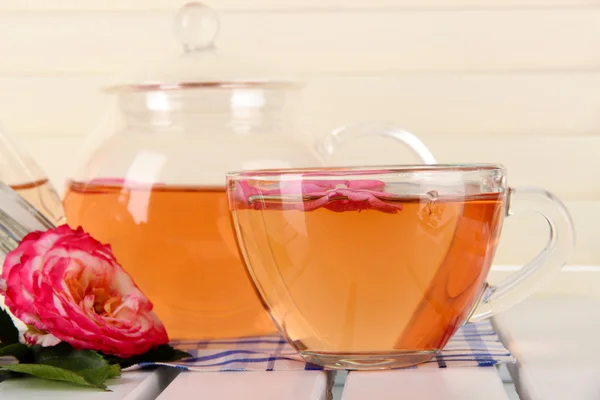 Kettle and cup of tea from tea rose on napkin on wooden background — Stock Photo, Image