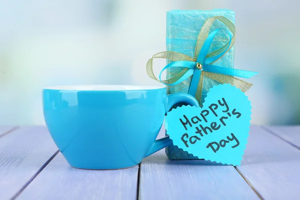 Étiquette Happy Fathers Day avec boîte cadeau et tasse, sur table en bois, sur fond clair — Photo