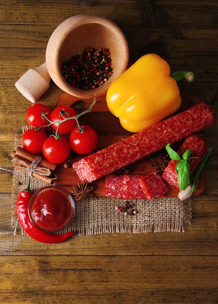 Leckere Salamiwurst und Gewürze auf Holzgrund — Stockfoto