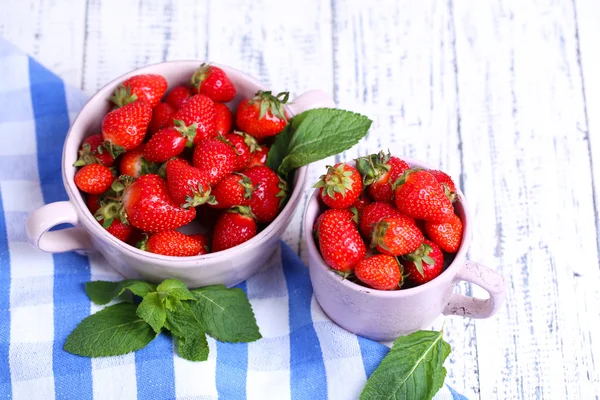 Maturi dolci fragole in pentola e la tazza su sfondo di legno a colori — Foto Stock