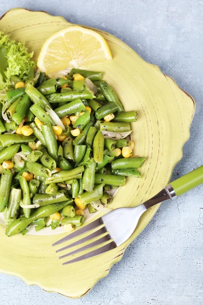 Salat mit grünen Bohnen und Mais, auf Teller, auf farbigem Holzgrund — Stockfoto