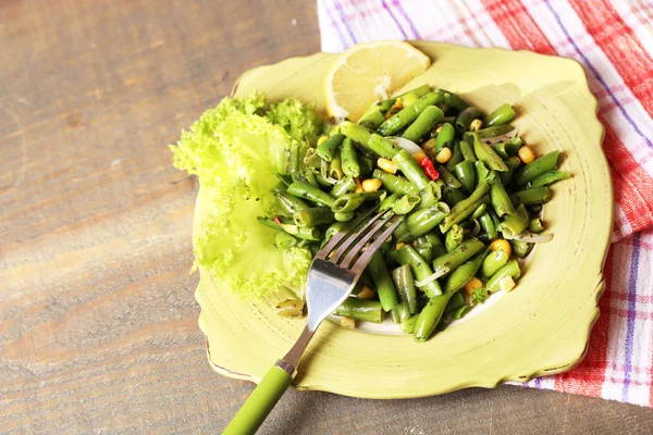 Insalata con fagiolini e mais, su piatto, su sfondo di legno a colori — Foto Stock