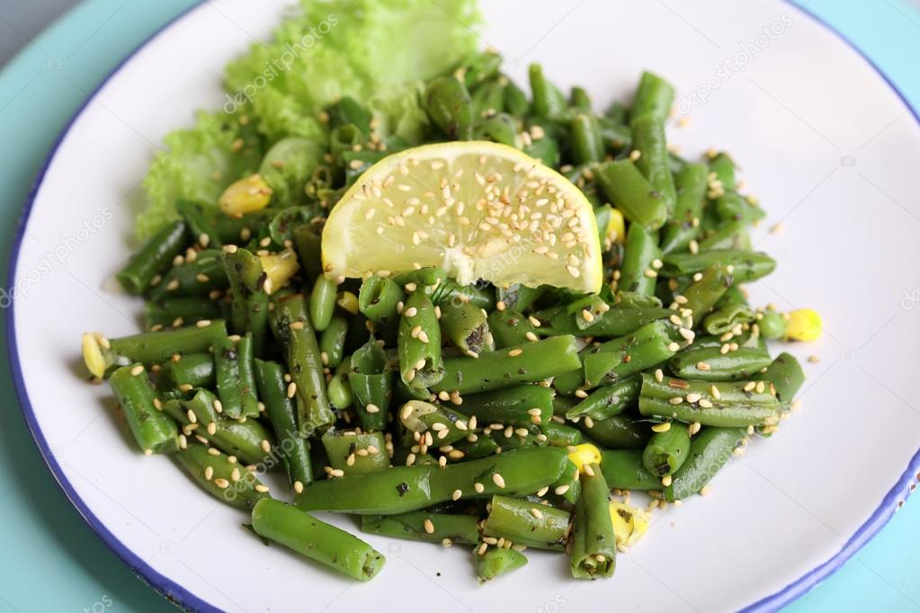 Salad with green beans and corn, sesame seeds on plate, on color wooden background