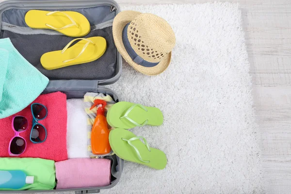 Maleta con cosas en alfombra blanca en el suelo para viajar a algún lugar cerca del agua para pasar las vacaciones de verano —  Fotos de Stock