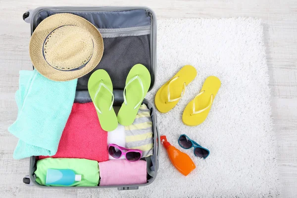 Maleta con cosas en alfombra blanca en el suelo para viajar a algún lugar cerca del agua para pasar las vacaciones de verano — Foto de Stock