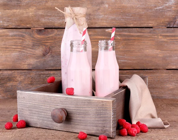 Botellas de sabrosas bebidas batidas de frambuesa sobre fondo de madera rosa gris —  Fotos de Stock