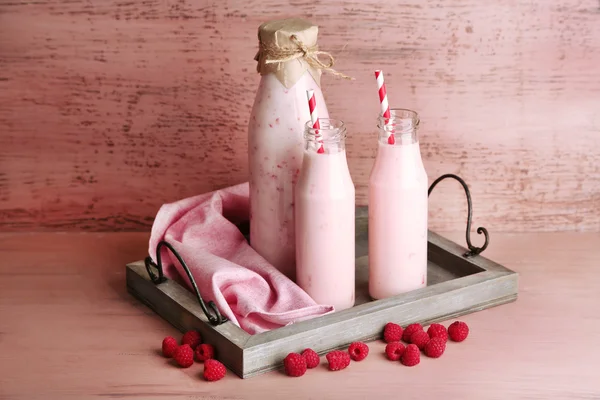 Bottiglie di gustose bevande al lampone frullato su sfondo di legno rosa — Foto Stock