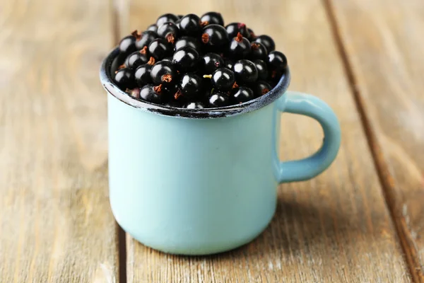 Ripe blackcurrants in mug on wooden background. — Stock Photo, Image