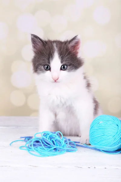 Cute little kitten playing with thread ball on light background — Stock Photo, Image
