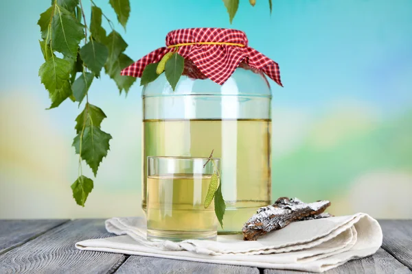 Verre et grand flagon de sève de bouleau frais sur une table en bois sur fond nature — Photo