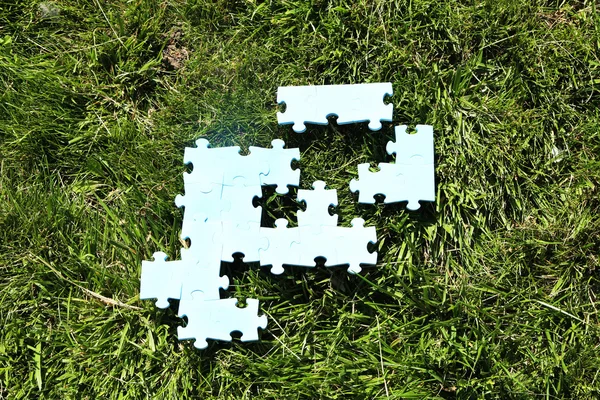 Puzzle kousky na zelené trávě pozadí. koncept zelených ploch — Stock fotografie