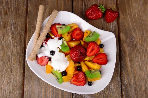Frischer Obstsalat mit Eis auf Teller und Beeren auf Holzgrund — Stockfoto