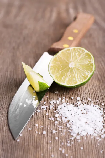 Bodegón con lima fresca, cuchillo y sal sobre una vieja mesa de madera — Foto de Stock