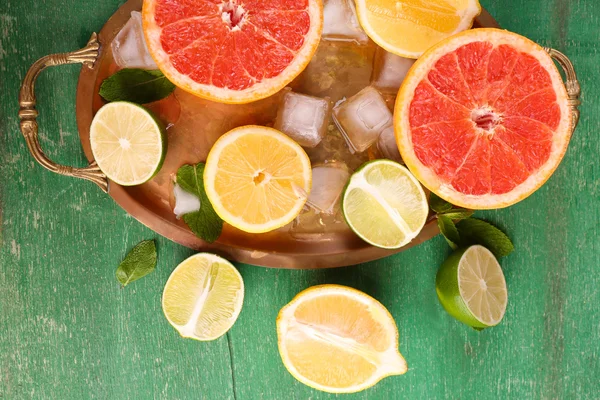 異なるスライスしたジューシーな柑橘系の果物氷トレイ、緑の木製テーブル上で — ストック写真