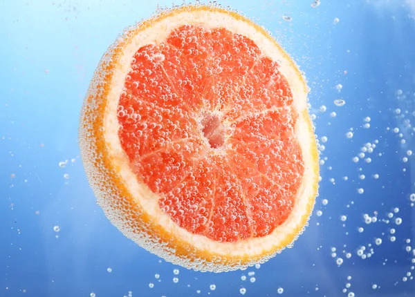 Frische Grapefruit im Wasser mit Blasen auf blauem Hintergrund — Stockfoto