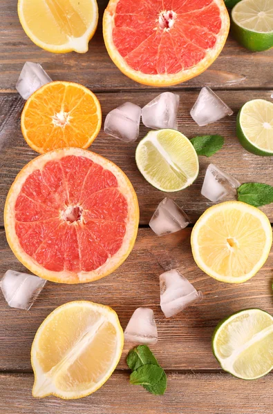 Olika skivad saftiga citrusfrukter med is på träbord — Stockfoto