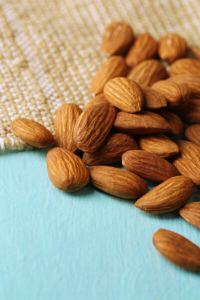 Almonds on color wooden table, on sackcloth background