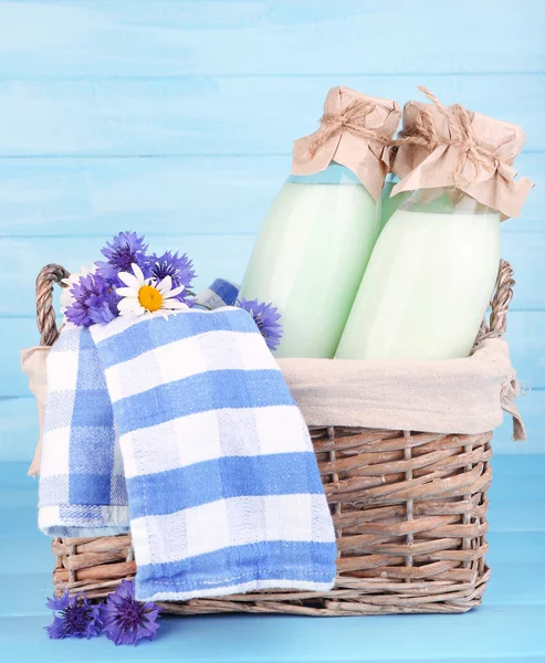 Bottles of milk and cornflowers in wicker basket on wooden background — Stock Photo, Image