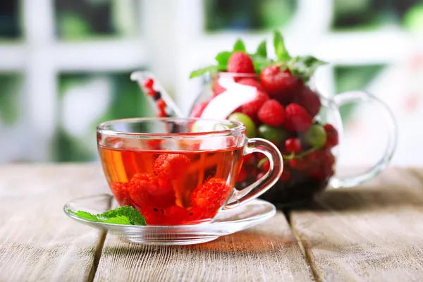 Tè rosso frutta con frutti di bosco in tazza di vetro, su tavolo di legno, su sfondo luminoso — Foto Stock