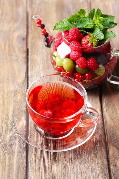 Té rojo de frutas con bayas silvestres en taza de vidrio, sobre fondo de madera —  Fotos de Stock