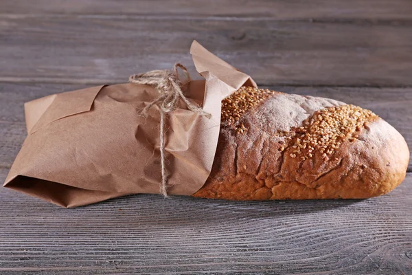 Frisch gebackenes Brot in Papier gewickelt, auf Holzgrund — Stockfoto